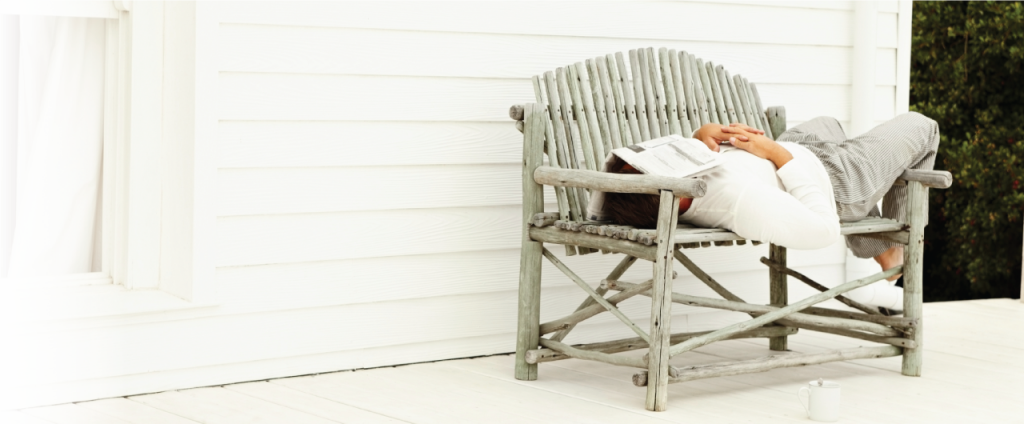 Man laying on a wooden bench, with a newspaper laying over his face