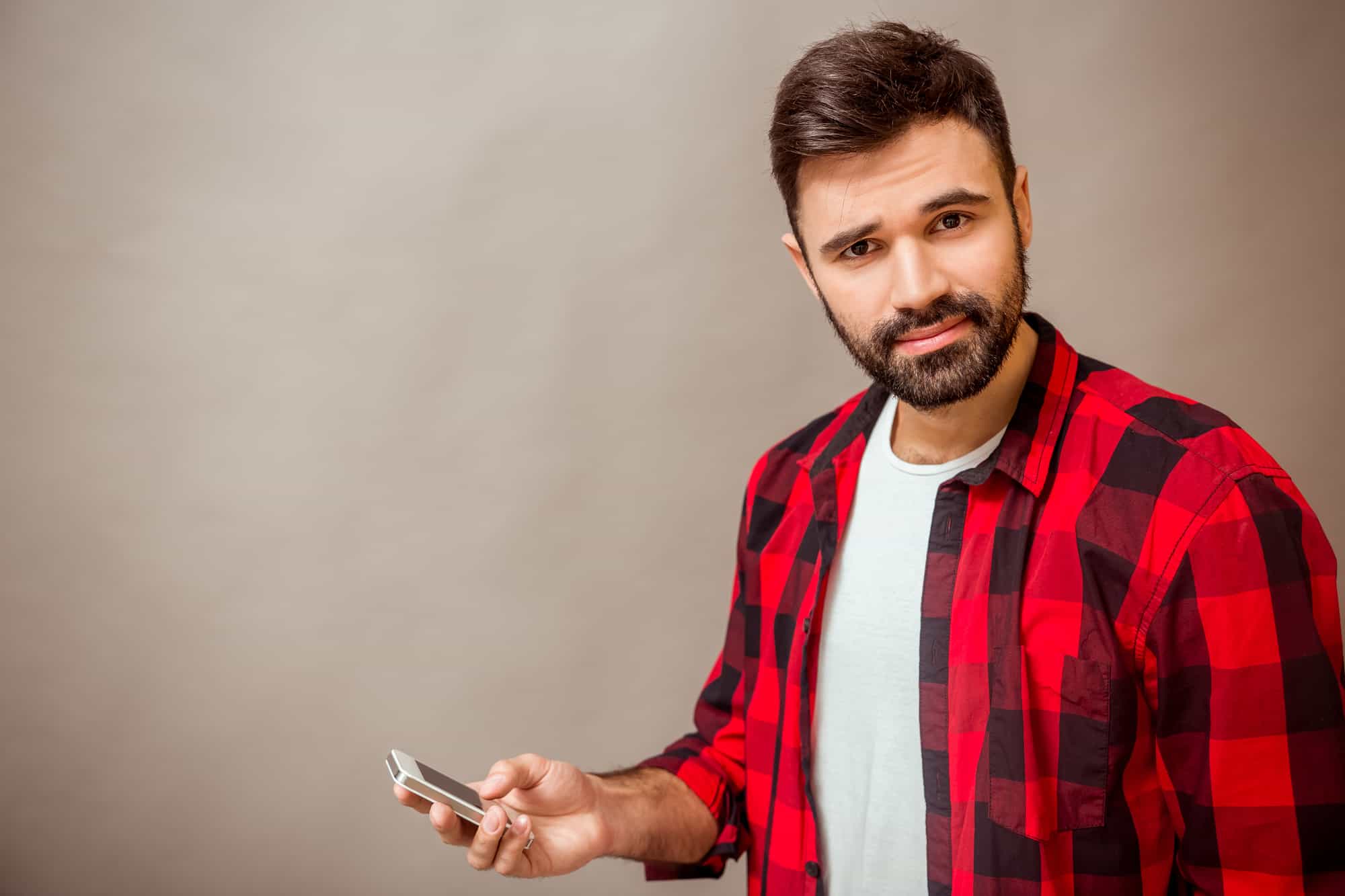 Beautiful young man in a checkered shirt, smartphone in hand, expressing